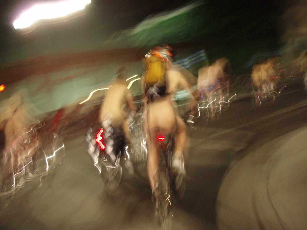 A blurred action photo of people riding bikes at night with no clothes on .