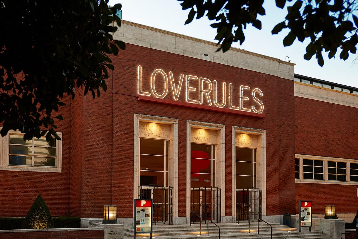 The front facade of the Portland Art Museum with a neon art sign over the door that read "LOVERULES"