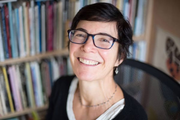 Poet Martha Silano sits in an office in front of a shelf full of books. 
