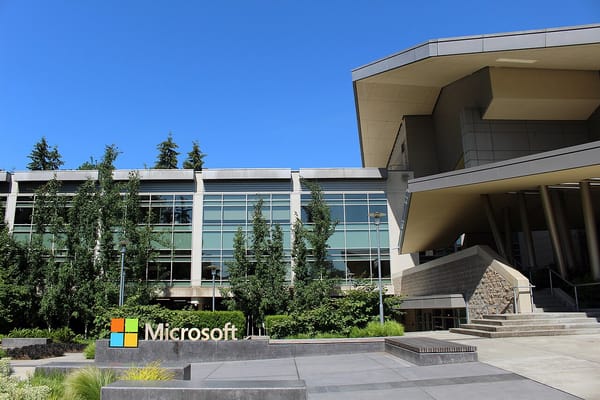An office building surrounded by evergreen trees, with a sign showing the Microsoft logo.