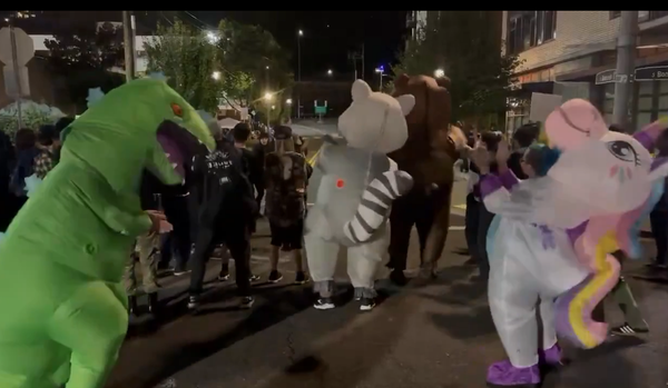 Protesters in inflatable Godzila, racoon, and unicorn suits dance in front of an ICE facility.